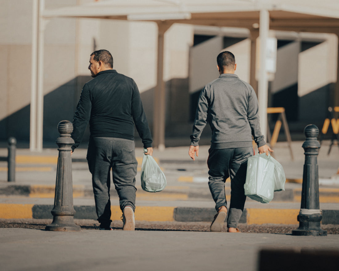 Two people carrying bags on a sunny street in Kuwait City
