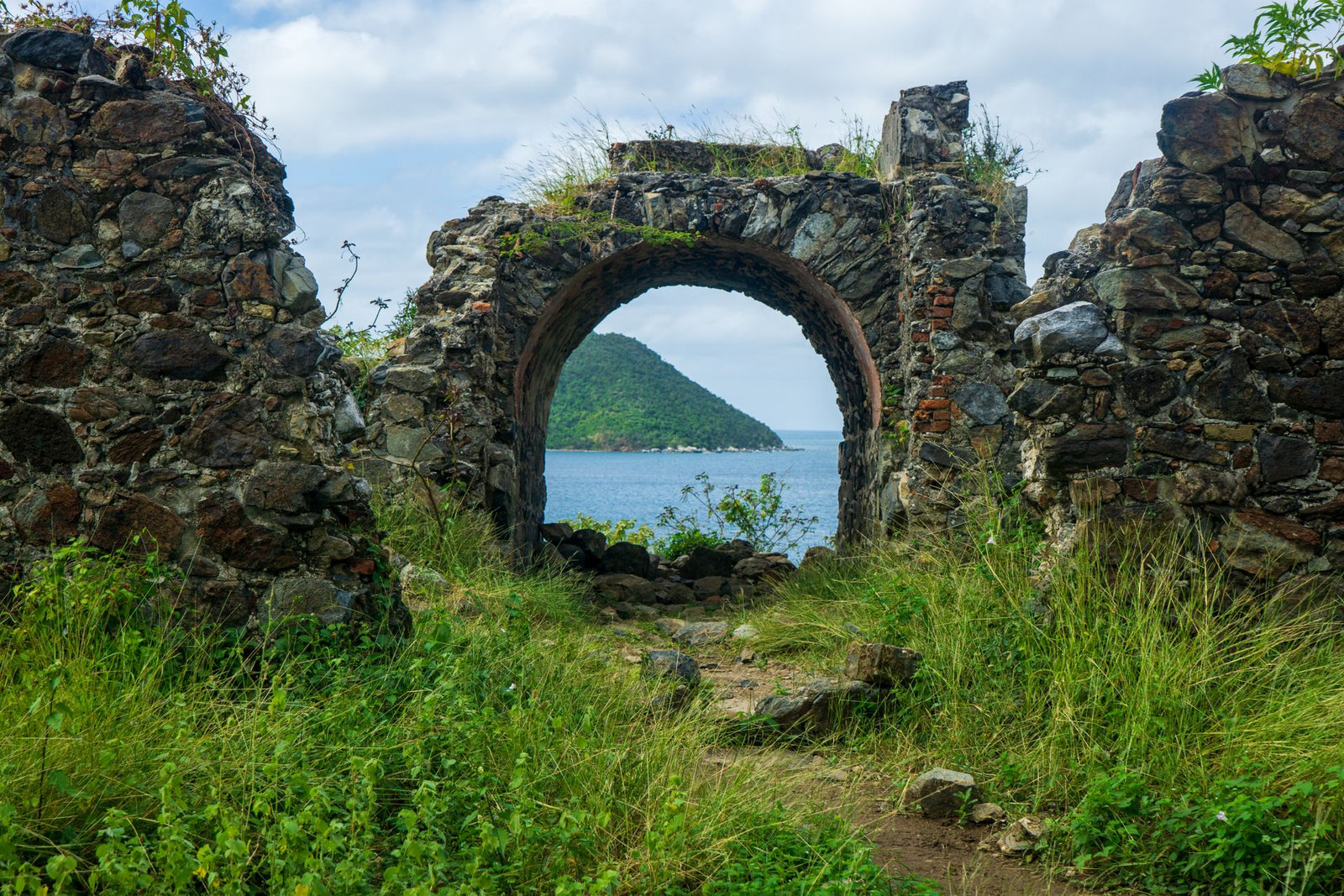 Scenic view through ancient stone ruins by the ocean with lush greenery.
