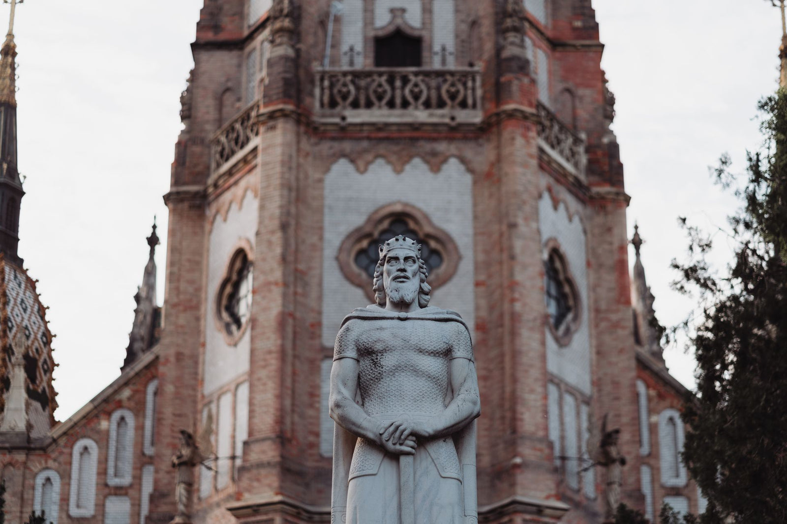 A striking statue in front of a gothic-style church in Budapest, showcasing historical architecture.