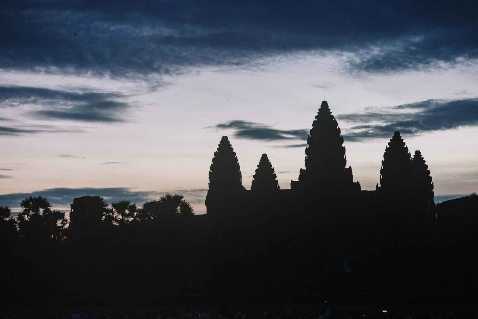 Silhouette of Angkor Wat temple at dusk with dramatic sky.