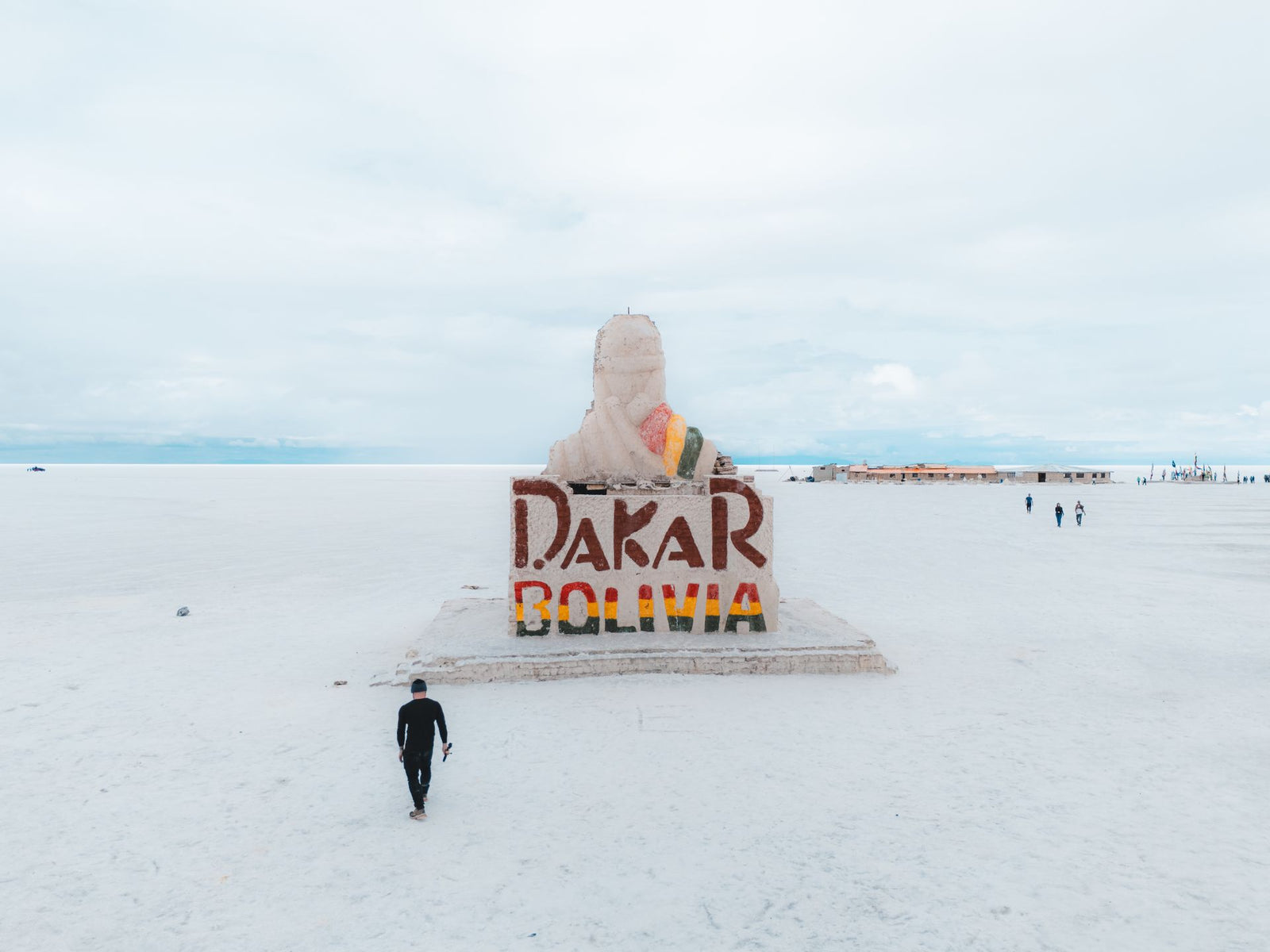 A solitary traveler approaches the Dakar Rally Monument in the vast Salar de Uyuni, Bolivia.