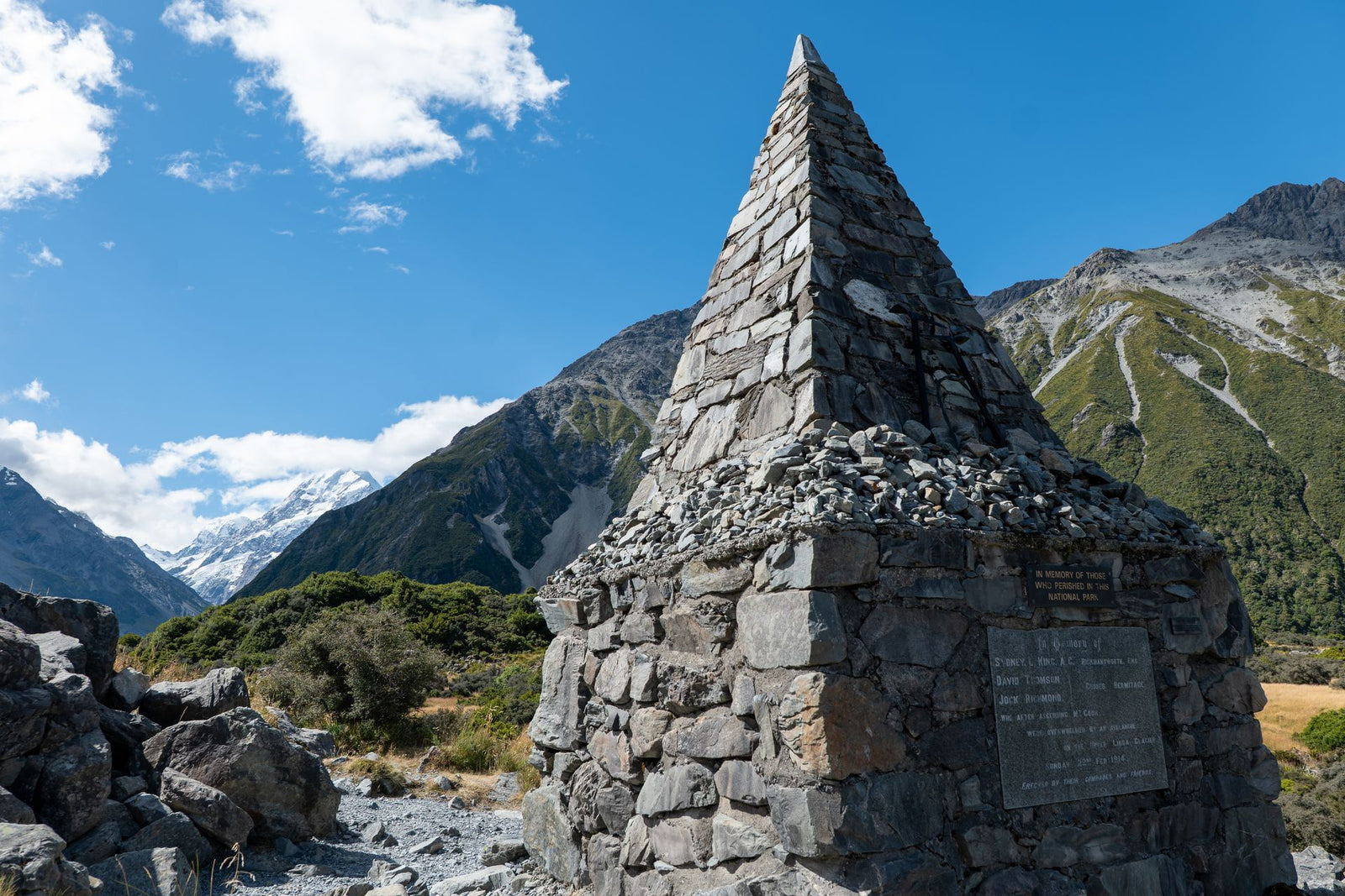 A stone cairn stands beneath clear blue skies at Aoraki/Mount Cook, showcasing New Zealand's stunning mountain landscape.