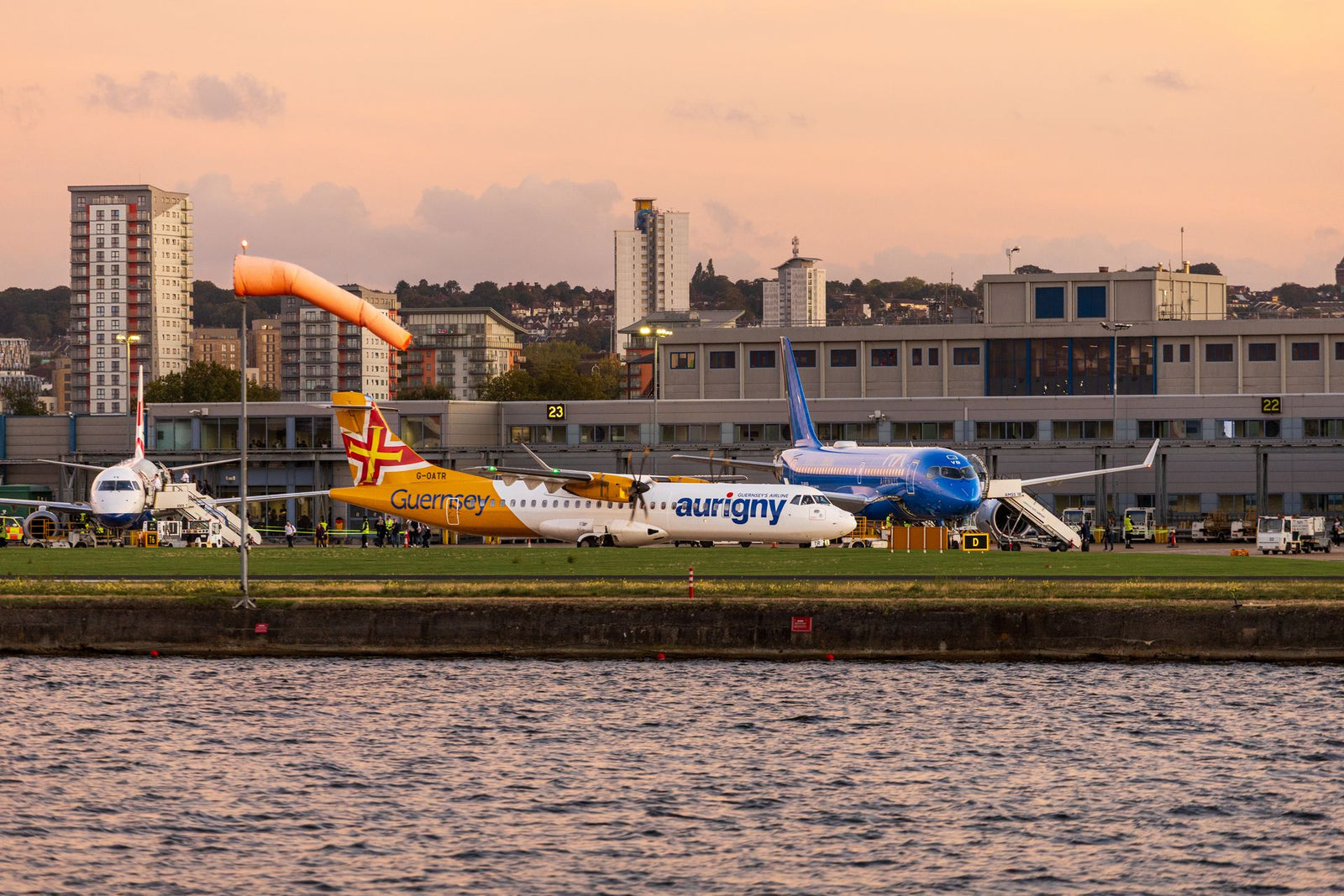 Airplanes parked on runway at airport terminal with cityscape backdrop during sunset.