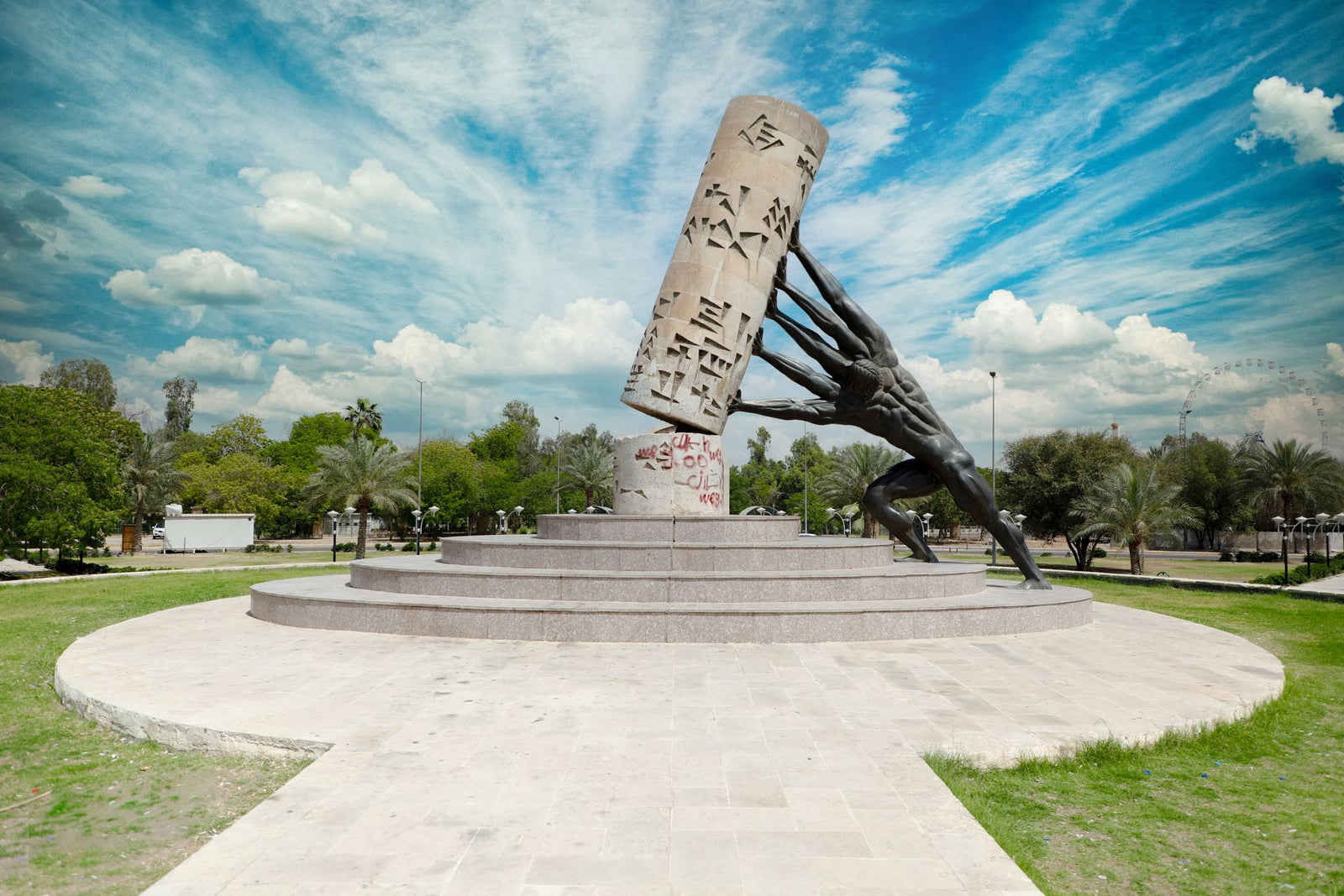 Vandalized sculpture in a Baghdad park under a vibrant blue sky.